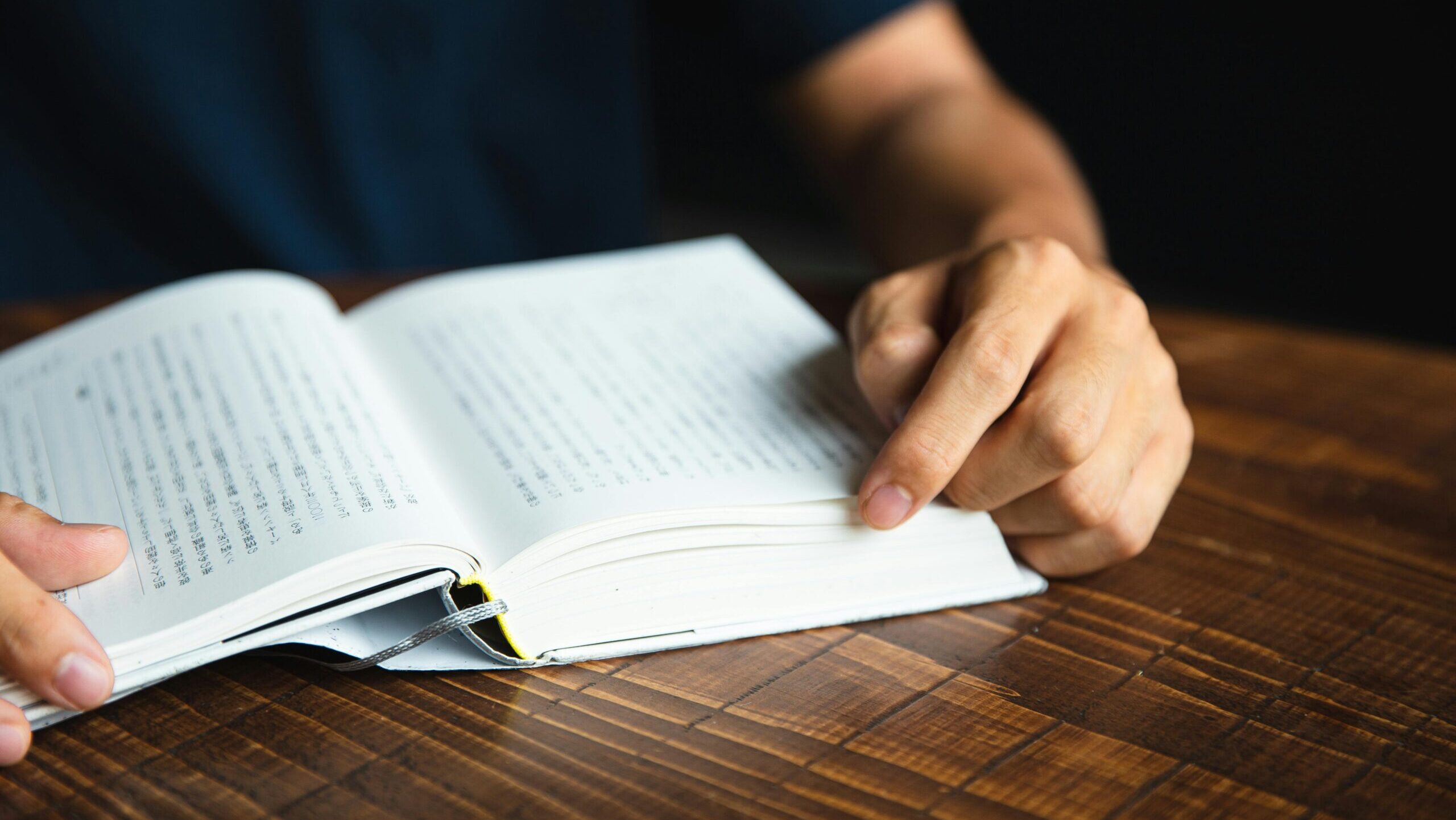 Crop anonymous male wearing dark shirt sitting at round table and enjoying good novel in hardcover book