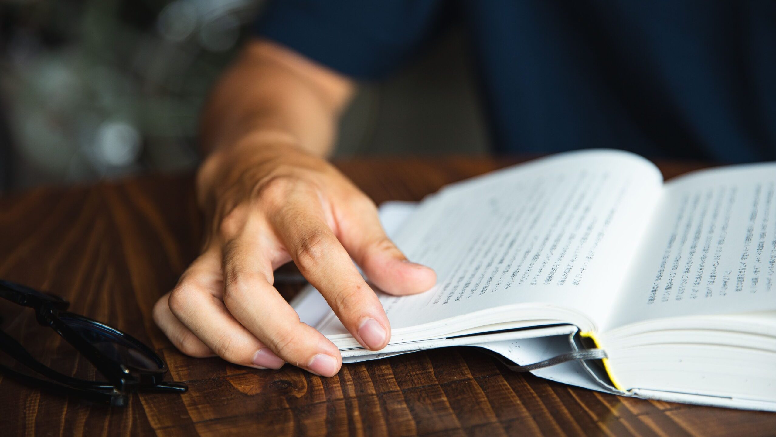 Crop anonymous male in casual shirt sitting at round table and reading interesting book